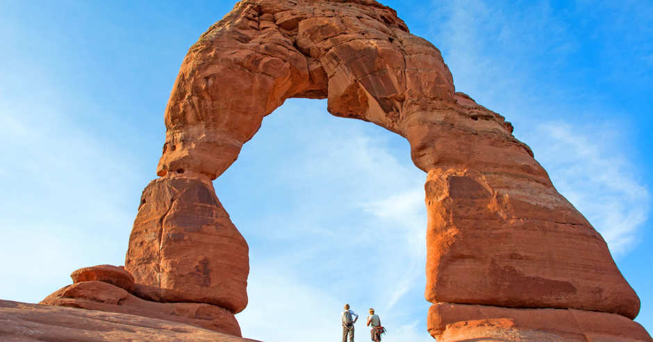 Two people under the Delicate Arch in Arches National Park in Utah