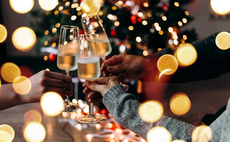A group of people clink champagne flutes surrounded by twinkling Christmas lights