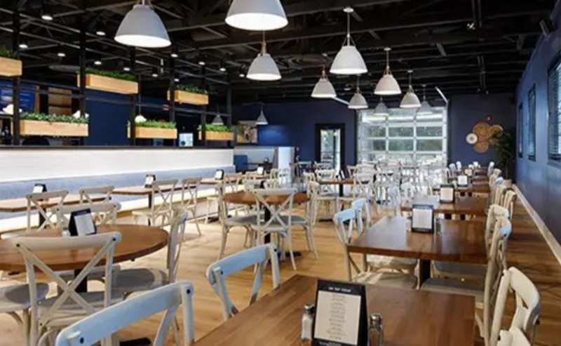 Bright, modern dining area at Bounty Farmhouse Kitchen & Taphouse in Fayetteville, NC, featuring wooden tables, white chairs, and soft pendant lighting.