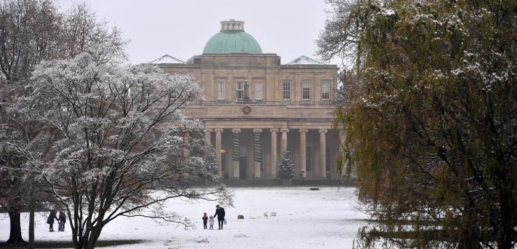 Visitors walking their dog through a snow filled park in Cheltenham