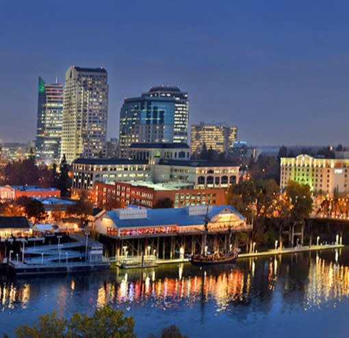 An evening lights photo with the Old Sacramento Waterfront in the foreground and Downtown skyline in the background