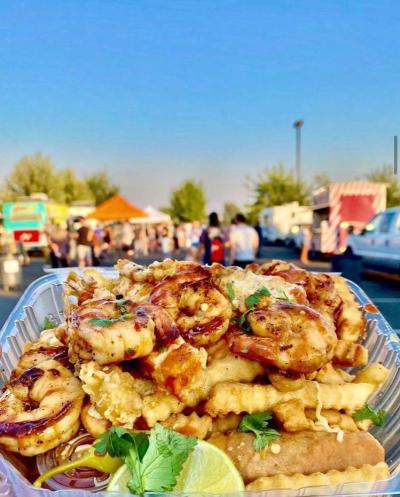 Plate of fries covered in shrimp and cheese with food trucks in the background