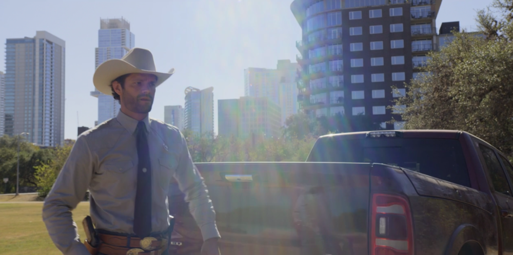 Walker screengrab, showing Walker in a white cowboy hat and blue shirt and tie. He stands in front of a truck in Duncan Park. The city skyline is visible behind him