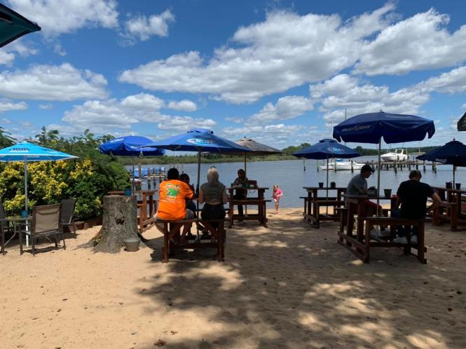 A group of tables wit umbrellas on a beach with a water view.