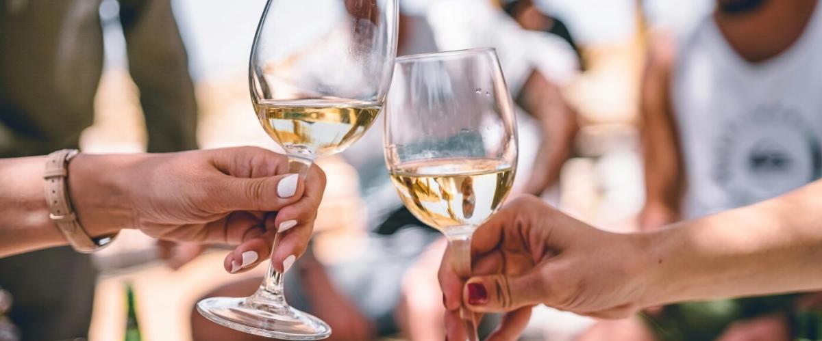 Two hands holding two glasses half filled with white wine coming together for a toast.