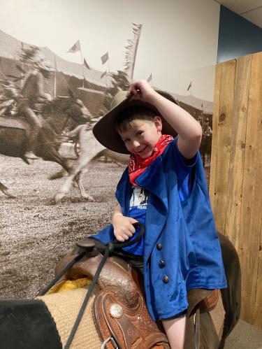 At the Buffalo Bill Museum a young child dresses up as a cowboy and rides a play horse