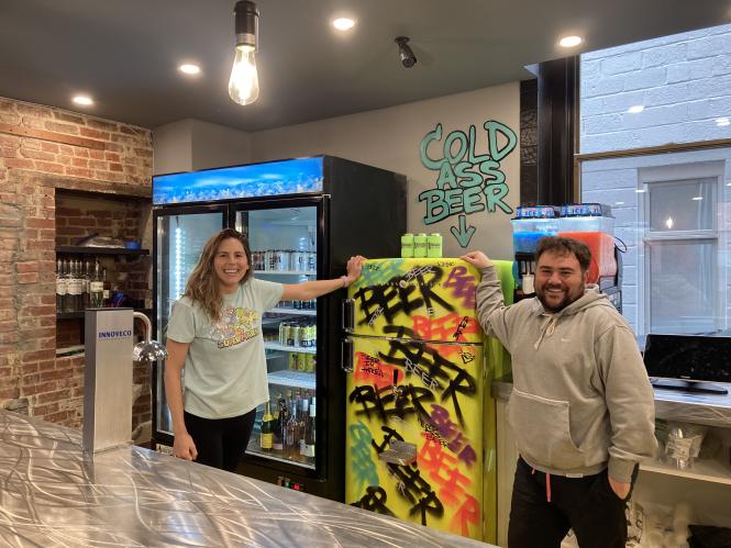 owners Casey and Eli stand in front of a beer fridge