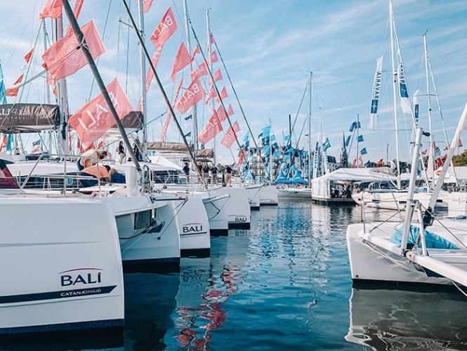 Sailboats and catamarans lined up in the water with flags flying up the mast.