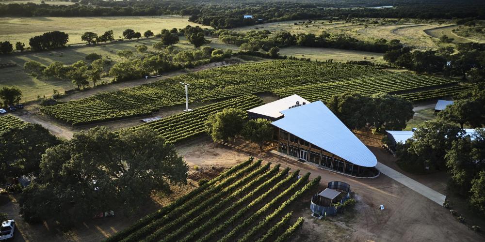 Birds-eye view of William Chris Vineyards - large metal building surrounded by rolling Hill Country and green rows of grape vines.
