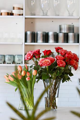 Two vases of flowers, tulips and roses, in front of shelves of merch