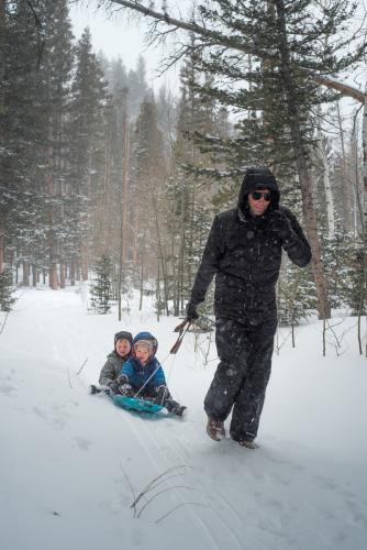 man holding sled with two children in winter
