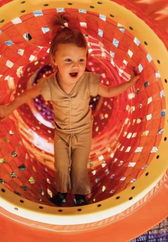 A little girl has a look of wonder on her face as she plays in an orange mesh tunnel.