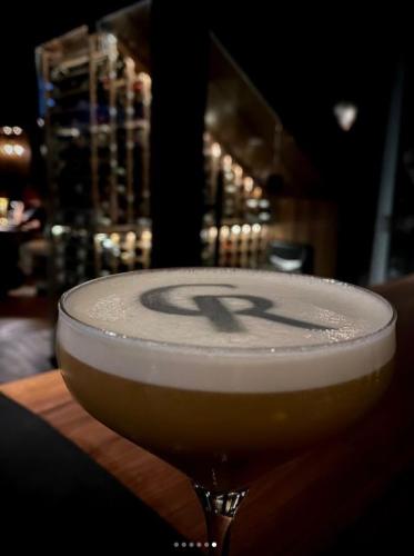 Cocktail with foamy top and initial CR in the foam, sitting on a counter.