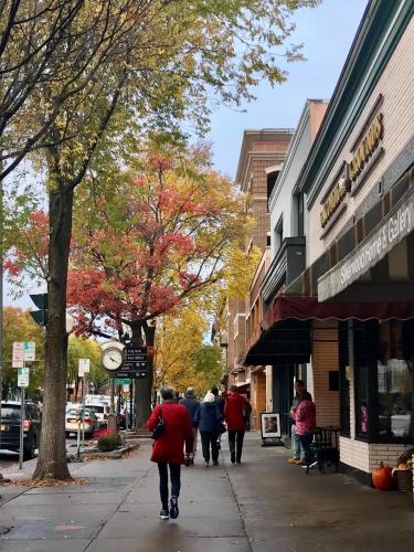 Woman in red coat walking on Broadway sidewalk in autumn.