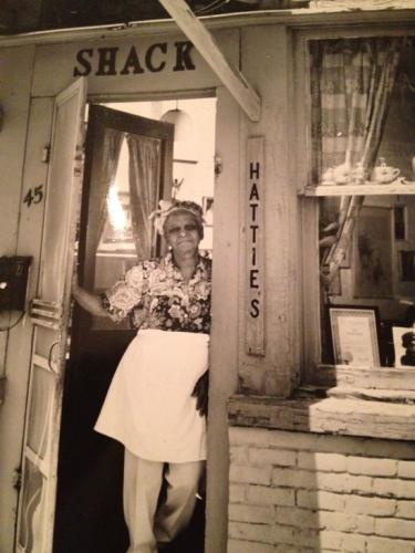 B&W photo of Hattie standing in doorway of her restaurant wearing a white apron