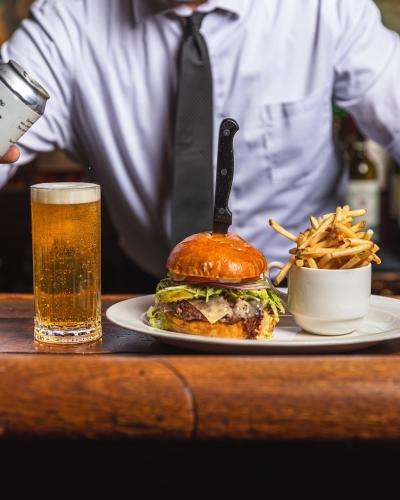 man pouring beer into glass, burger and fries sit next to glass of beer