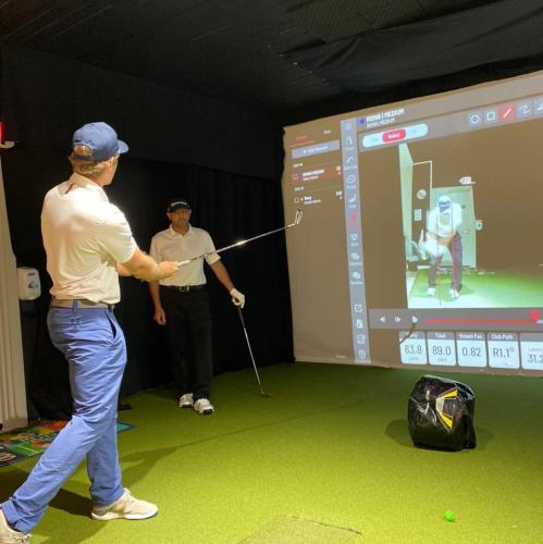 Two men using the golf simulator with one taking a swing