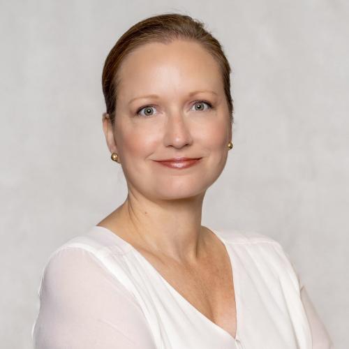 Professional headshot of woman with hair pulled back, smiling, wearing a white blouse.