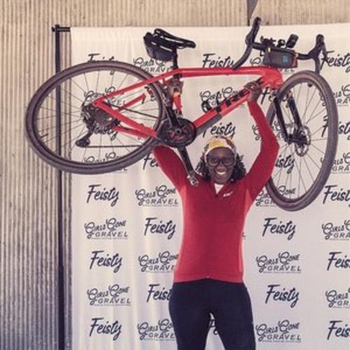 A person holds a gravel bike over her head and smiles