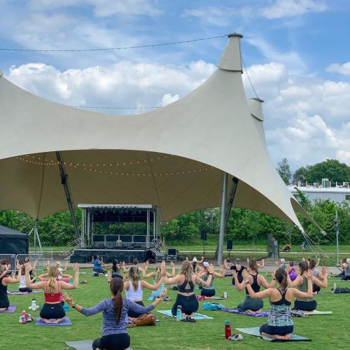 Several people practicing yoga on an outdoor green space in front of a large canopy