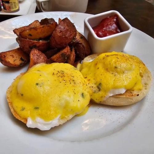 Two eggs Benedict with roasted potatoes on a white plate