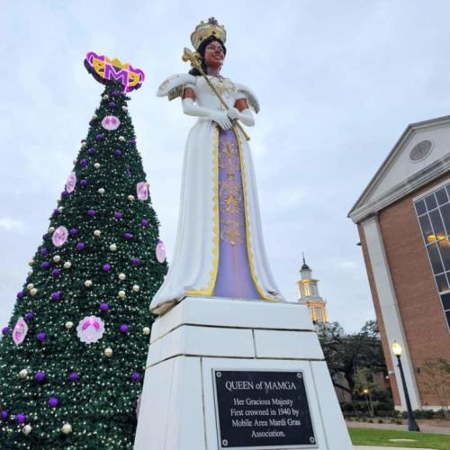 Statue of a Black Mardi Gras queen in a park in front of a giant tree decorated with Mardi Gras beads