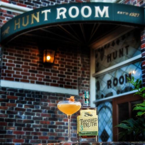 A cocktail next to a bottle of liquor in front of the hunt room entrance