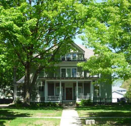 Large home set back from street and surrounded by bright green trees and lawn