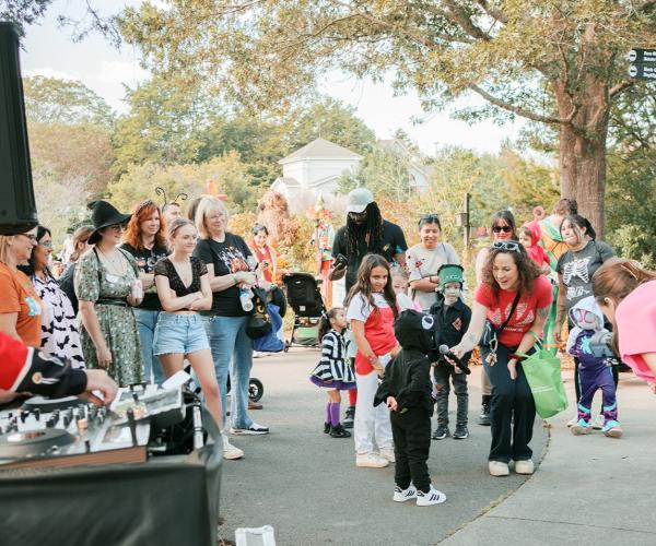 Families in Halloween costumes enjoy Little Monsters Mash at Huntsville Botanical Garden, with a DJ and children participating in activities.