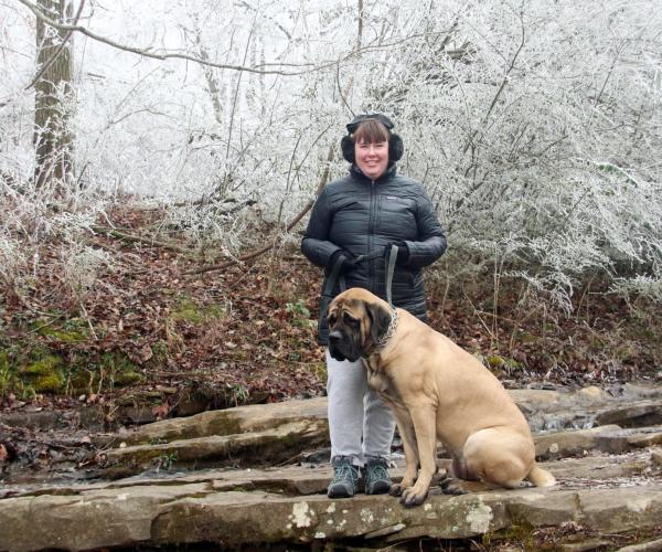 A woman stands with a leashed dog on a rocky trail at Monte Sano State Park, surrounded by trees and branches covered in ice.
