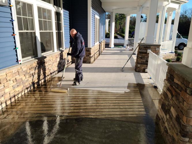 Employee varnishing front porch floor in front of blue house.