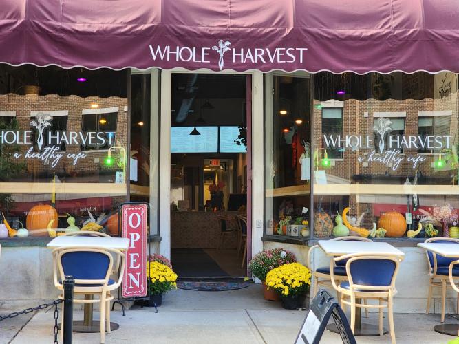 Exterior shot of storefront with burgundy awning, outdoor tables and potted mums