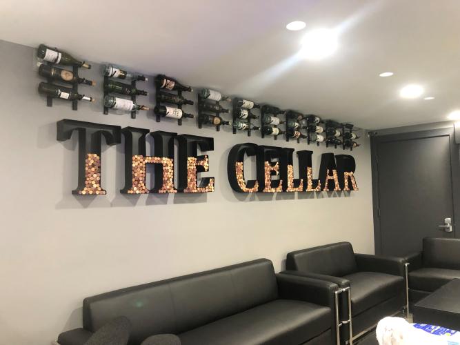 The Cellar wall sign with wine bottles displayed over it and black couches underneath