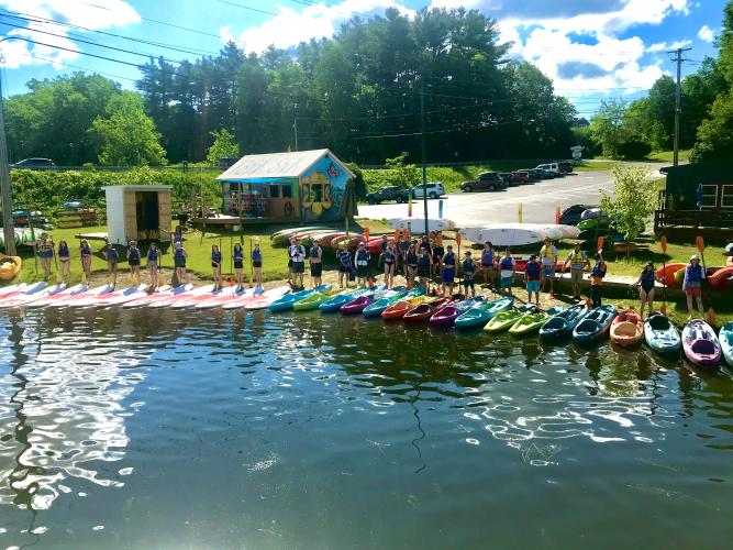 Group of people lined up on shore with paddleboards and kayaks