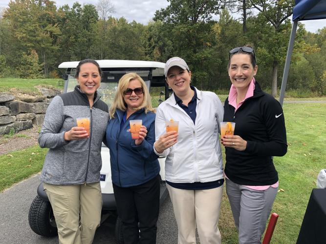 MaryJo and foursome holding up drink glasses with golf cart behind them