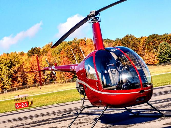 Red helicopter on the ground with fall foliage in the background