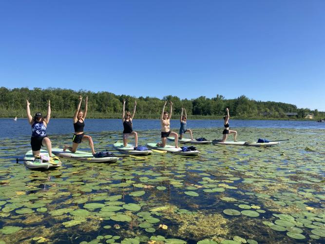 Six women on SUPs on the lake with arms over their heads in Yoga pose