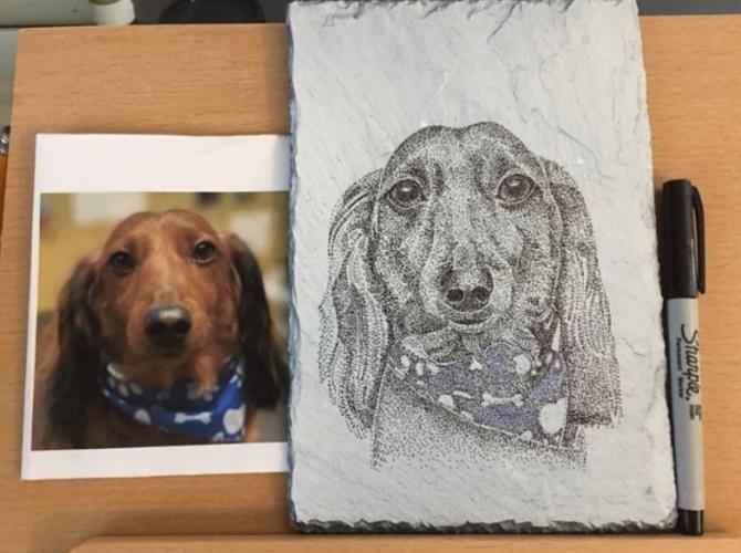 Photo of dog with etching on slate next to it