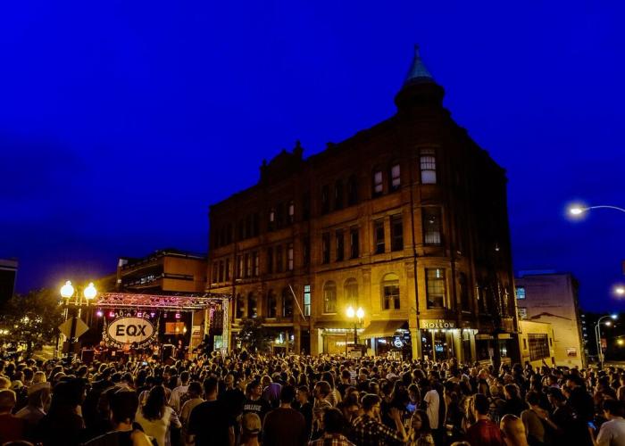 Evening event with large crowd, dark blue sky and EQX sign in front of a building