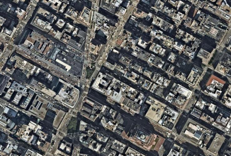 Satellite aerial view of Manhattan city blocks showing Broadway's diagonal path slicing through the otherwise rigid rectangular street grid, creating triangular intersections and irregular block shapes between densely packed buildings.