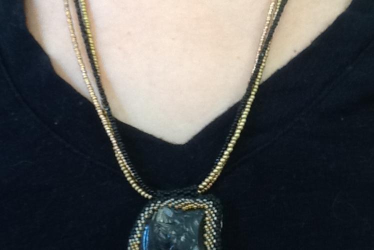 necklace with a bezeled river rock in black and gold beaded chain