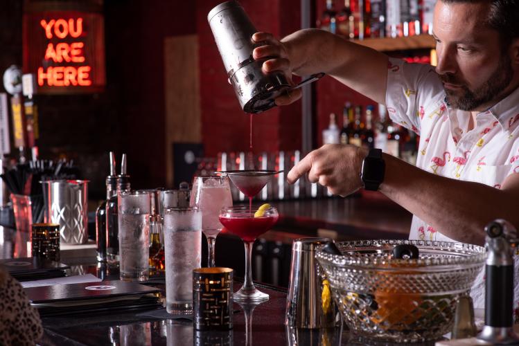 Bartender pouring drink from a strainer in dark bar