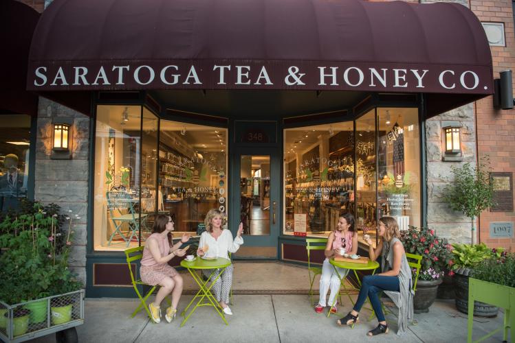 Group of 4 people enjoying tea and sitting on green chairs outside of Saratoga Tea & Honey