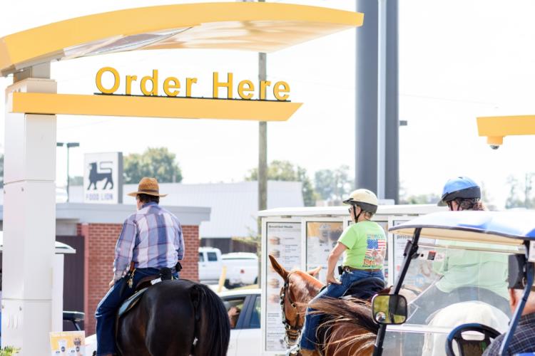 Two riders on mules at a McDonald's drive-thru in Benson, NC during Benson Mule Days.