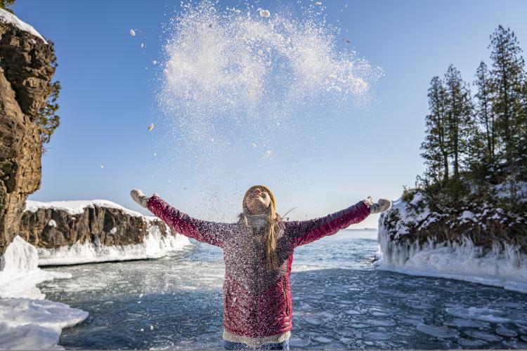 A young woman celebrates winter by throwing snow up in the air