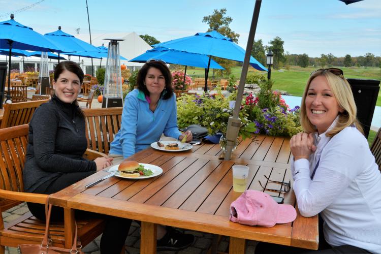 3 women sitting on patio at table at National under blue umbrella