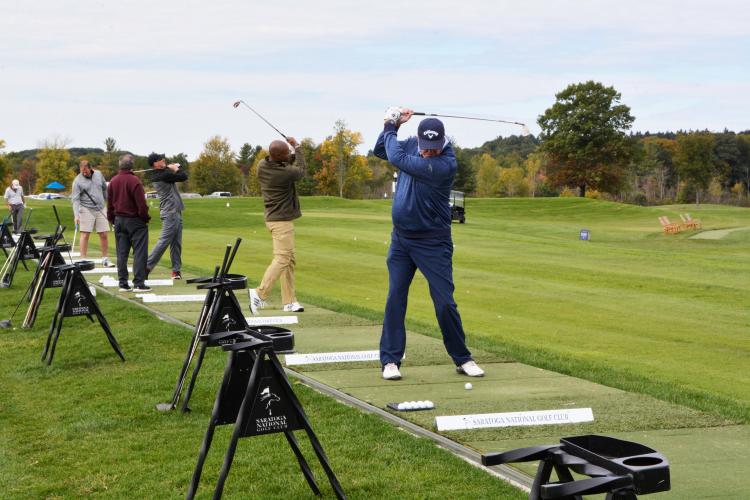 Four golfers lined up at the driving range taking practice swings