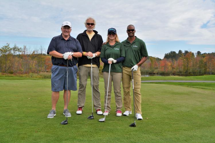 Foursome from the Saratoga Hampton Inn standing side by side with golf clubs in front of them.