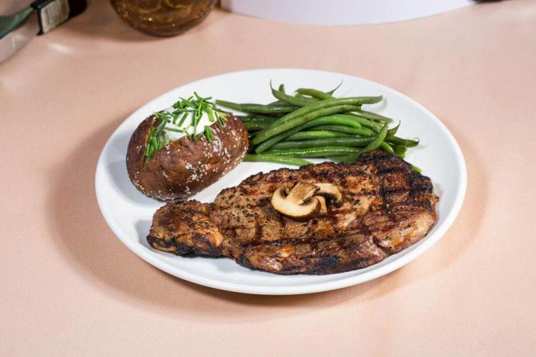 White plate on beige tablecloth with chicken flllet, green beans and baked potato