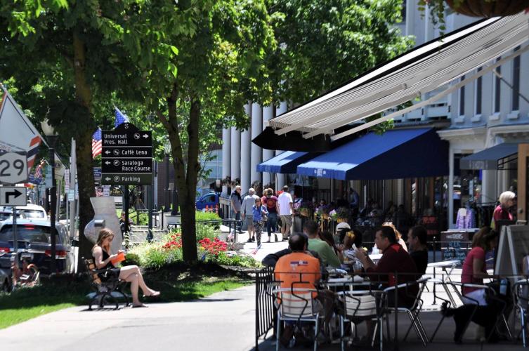 Broadway at lunchtime with people dining outside and sitting on park bench